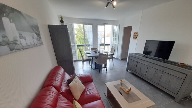 A modern living room with a red sofa, a wooden coffee table, a grey cabinet, and a television. - Charming T2 city center - 2 guests (La Roche-Posay)