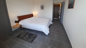 A bedroom with a bed, bedside lamps, a door, a painting, and a patterned rug. - Charming T2 city center - 2 guests (La Roche-Posay)