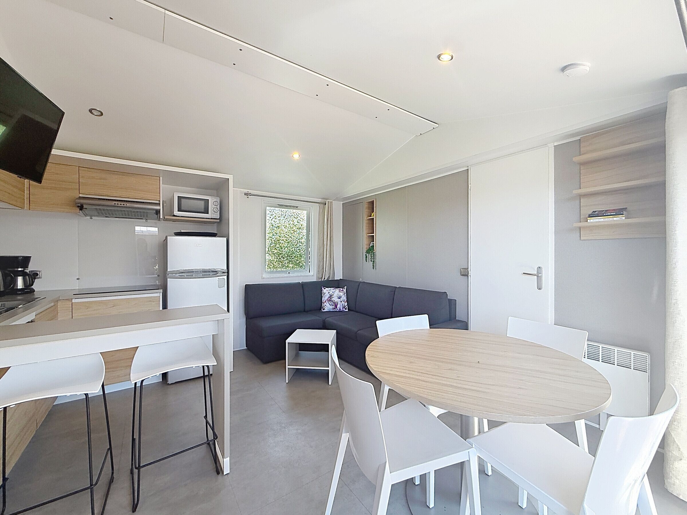 A modern kitchen with a dining area, a sofa, and a TV.