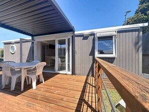 A modern cabin with a wooden deck, a dining area with plastic chairs, and a sliding glass door to a kitchen. - City mobile home, pets allowed - 4 guests (Jullouville)