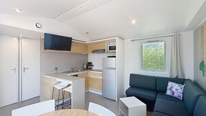 Kompakti oleskelutila, jossa on pieni keittiö, ruokailualue sekä oleskelualue, jossa on sohva ja televisio.