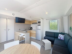 A compact living space with a kitchenette, a dining area, and a seating area with a sofa and a TV. - City mobile home, pets allowed - 4 guests (Jullouville)