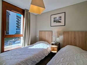Een hotelkamer met twee bedden, een raam met gordijnen, een ingelijste foto aan de muur en een nachtkastje met een lamp.