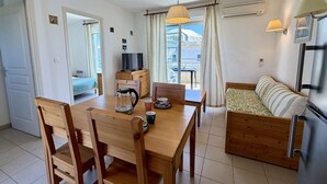 A compact living space with a wooden dining table, chairs, a sofa, a TV, and a kitchenette. - Ideal apartment beach access + pool (Poggio-Mezzana)