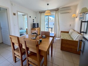 Ein gemütlicher Wohnraum mit Holztisch, Stühlen, einer Couch, einem Fernseher und einer Küchenzeile.