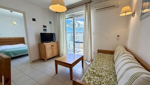 A room with a bed, a TV on a wooden cabinet, a sofa, a table, and a balcony with curtains. - Ideal apartment beach access + pool (Poggio-Mezzana)