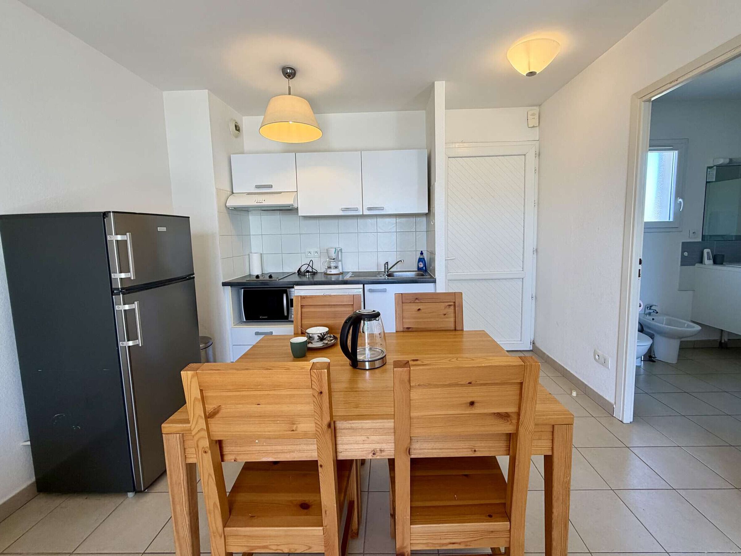 A compact kitchen with a black refrigerator, white cabinets, a wooden dining table, and a coffee maker.