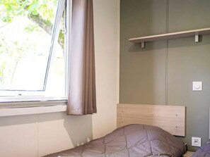 Ein Zimmer mit einem Bett, einem Vorhangfenster, einem Wandregal und einem Lichtschalter.