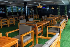 A restaurant with wooden tables and chairs, green artificial grass flooring, and hanging pendant lights. - Ocean Front Hotels Enuguu (Enugu)