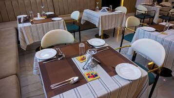 A dining area with tables set for two, featuring striped tablecloths, white plates, cutlery, and a glass of water.