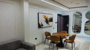 Um interior moderno com uma sala de jantar, destacando uma mesa redonda e quatro cadeiras, um sofá cinza e um grande quadro abstrato na parede.