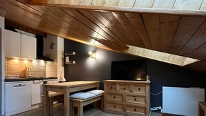 Une cuisine compacte avec un plafond en bois, une table à manger, un meuble encastré et un téléviseur fixé au mur.