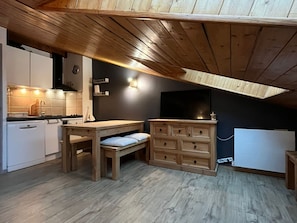 A compact kitchen with a wooden ceiling, a dining table, a built-in cabinet, and a TV mounted on the wall. - Comfortable apartment - 4 guests (Châtel)