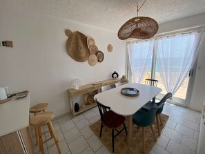 Un coin repas avec une table blanche, deux chaises, un buffet en bois et un luminaire suspendu au plafond, fait de fibres tressées.