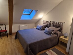 Ein Schlafzimmer mit Dachfenster, einem Bett mit Kissen, einem Sessel, einem Nachttisch mit Lampe und einem Heizkörper.