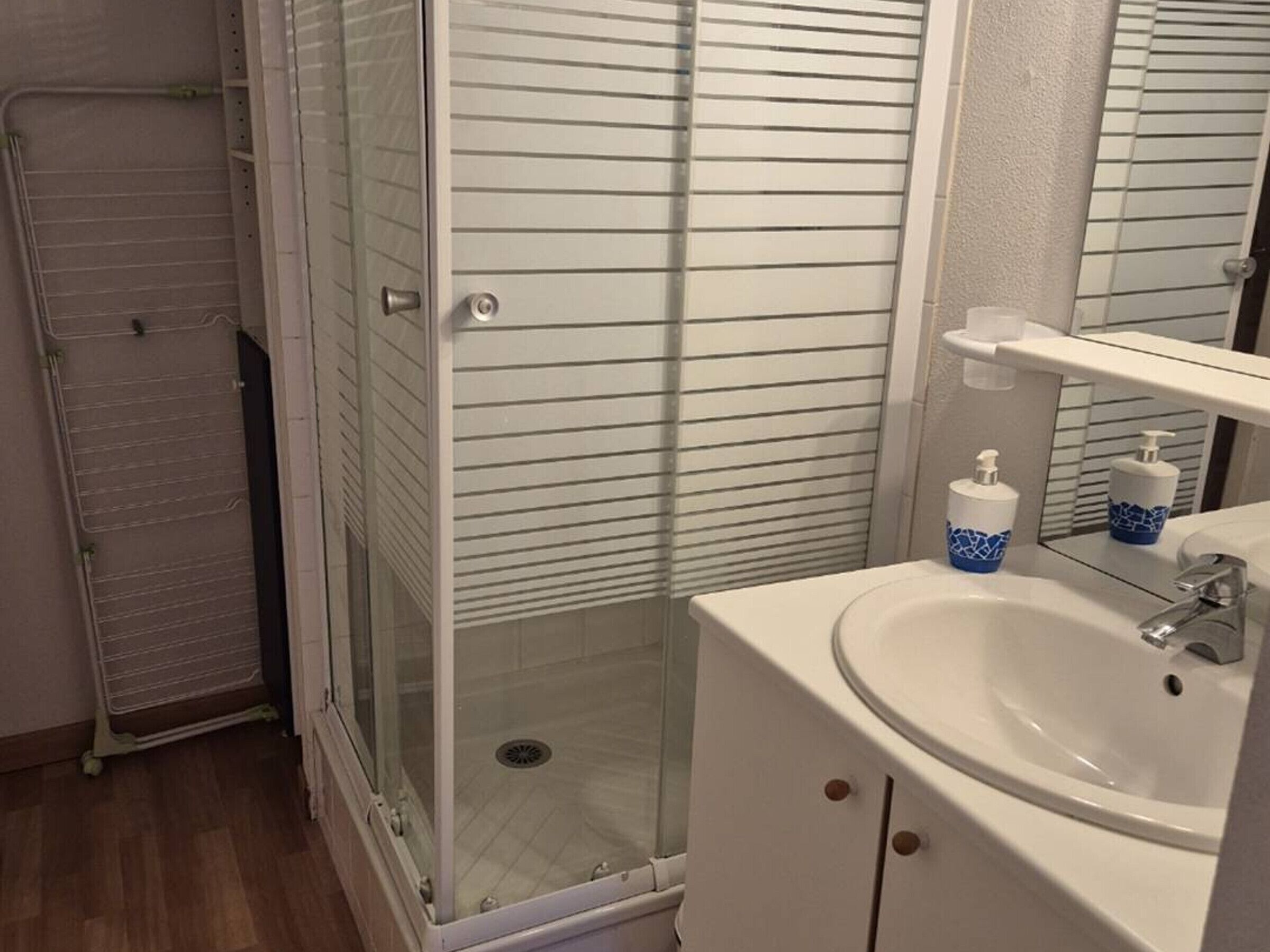 Une salle de bain avec une douche à parois de verre, un lavabo avec un miroir et des articles de toilette posés sur le lavabo.