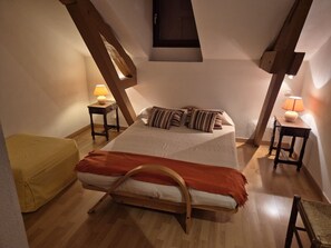 Une chambre à coucher avec un lit, deux tables de chevet, un banc en bois et une petite fenêtre.
