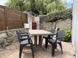 An outdoor patio with a table and four chairs, a stone wall, a wooden fence, and a red door. - Charming house near beach - 4 guests (Pleumeur-Bodou)