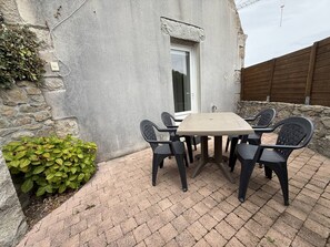 An outdoor patio with a table and chairs, a stone wall, and a wooden fence. - Charming house near beach - 4 guests (Pleumeur-Bodou)