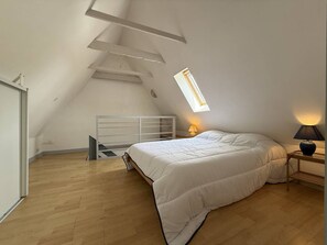 A bedroom with a sloped ceiling, a skylight, a bed, a bedside lamp, and a wooden floor. - Charming house near beach - 4 guests (Pleumeur-Bodou)