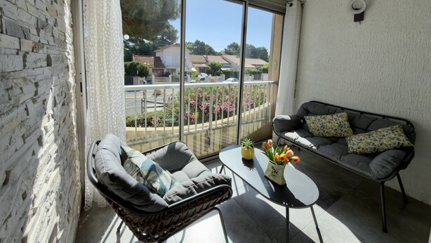 Ein Balkon mit einer Couch, Stühlen und einem Tisch mit Blumen.