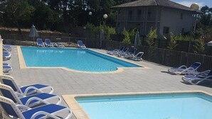 Uma piscina retangular com água azul, rodeada por espreguiçadeiras e uma cerca.