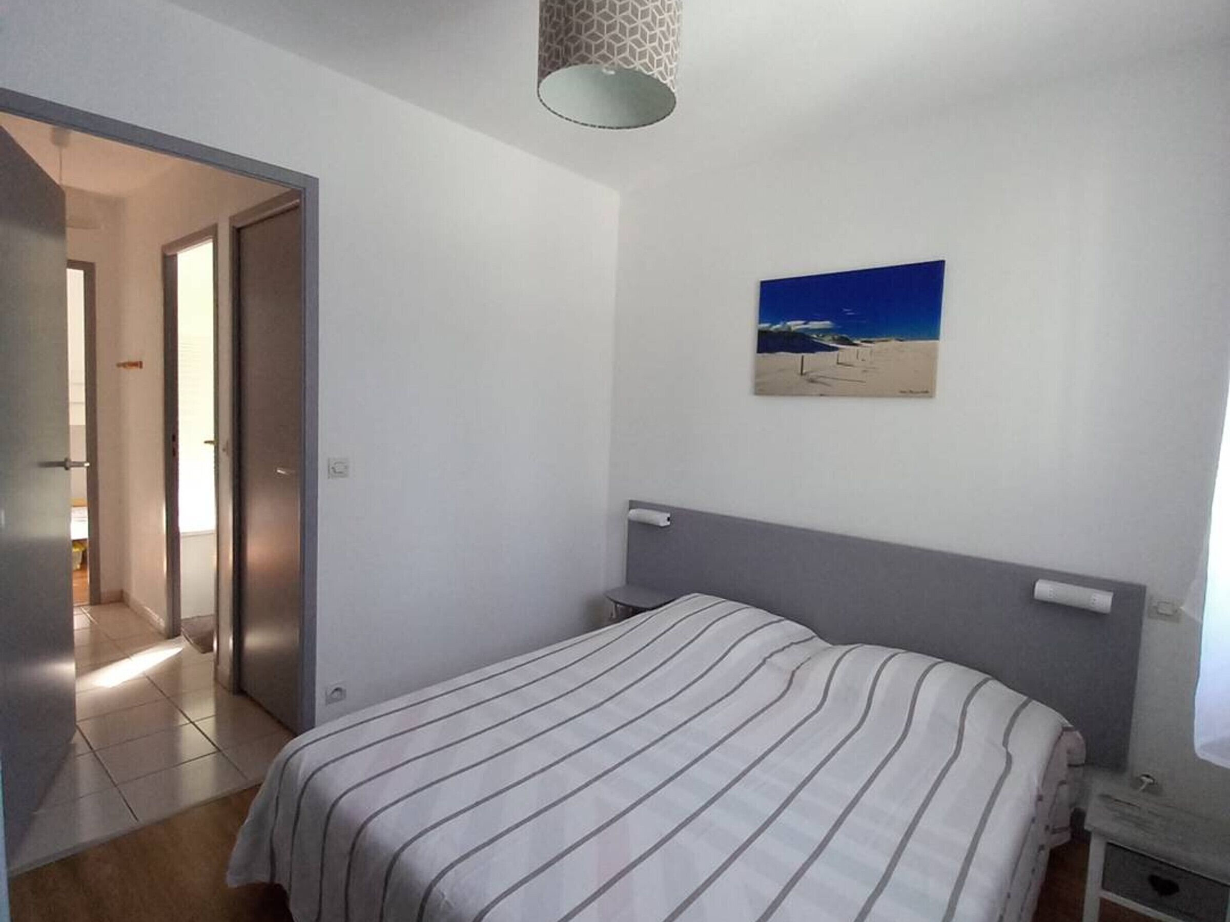 Une chambre à coucher avec un lit, un tableau, une porte et un luminaire.