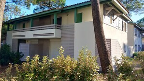 Um edifício de dois andares com varanda, cercado por árvores e arbustos.