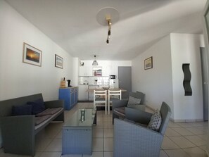 Een woonkamer met een bank, fauteuil en salontafel, een kitchenette met een magnetron, en een eethoek met een tafel en stoelen.