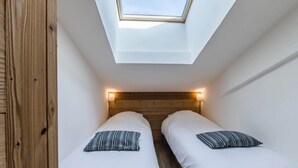 A small, modern bedroom with two beds, a skylight, and wooden headboard. - Renovated apartment, ski-in/ski-out - 5 guests (Val-d'Isère)