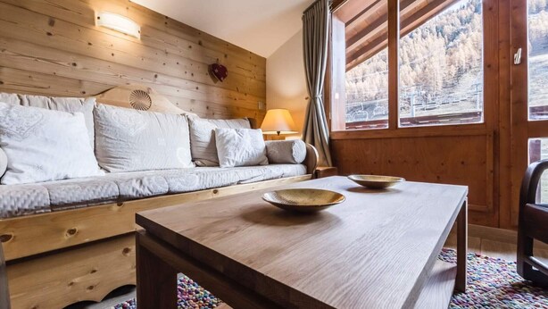 A cozy wooden room with a sofa, a table, and a window with a view of a forested area. - Renovated apartment, ski-in/ski-out - 5 guests (Val-d'Isère)
