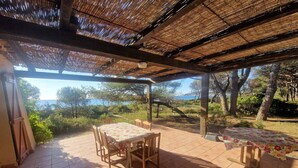 Eine überdachte Terrasse mit Tisch, Stühlen und einer Bank, mit Blick aufs Meer.
