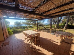 Eine überdachte Terrasse mit Tisch, Stühlen und einer Bank, mit Blick aufs Meer.