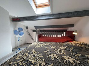 A bedroom with a skylight, a bed with a patterned bedspread, a standing fan, and a bedside lamp. - House with AC, near beach - 5 guests (Fleury-Saint-Pierre-la-Mer)