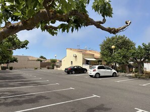 Un parking avec deux voitures, un bâtiment avec un toit en tuiles et des arbres.