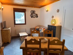 Ein gemütliches Zimmer mit Holztisch und -stühlen, einer Couch, einem Fenster mit Aussicht und Wanddekoration.