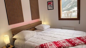 A bedroom with a bed, a window with a mountain view, a bedside lamp, and a framed picture on the wall. - New cozy apartment with balcony and private parking in Pralognan-la-Vanoise (Pralognan-la-Vanoise)