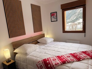 Ein Schlafzimmer mit einem Bett, einem Fenster mit Bergblick, einer Nachttischlampe und einem gerahmten Bild an der Wand.