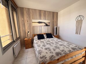 Ein Schlafzimmer mit einem Holzbett, einem Nachttisch, einer Wand-Klimaanlage, einem Fenster mit Ausblick und einer Wanddekoration aus Makramee.
