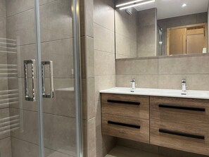 Ein modernes Badezimmer mit Duschkabine aus Glas, einem Holzbadschränken mit zwei Waschbecken und einem großen Spiegel darüber.
