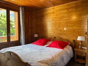 Ein Schlafzimmer einer Holzhütte mit einem Bett, zwei Nachttischlampen und einem Fenster mit Vorhängen.