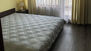 Ett hotellrum med en säng, ett nattduksbord, en luftkonditioneringsanläggning och utsikt genom tunna gardiner.