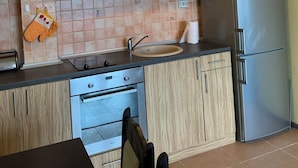 Ett modernt kök med träskåp, ett kylskåp i rostfritt stål, en inbyggd ugn och en hängande hylla för kastruller.