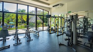 Ein Fitnessstudio mit großen Fenstern, Trainingsgeräten und Blick auf einen Pool und Grünflächen.