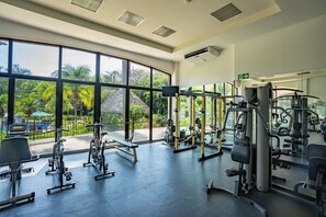 Ein Fitnessstudio mit großen Fenstern, Trainingsgeräten und Blick auf einen Pool und Grünflächen.