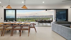 Ein moderner Essbereich mit einem großen Tisch für sechs Personen, einer Couch und Blick auf die Landschaft.