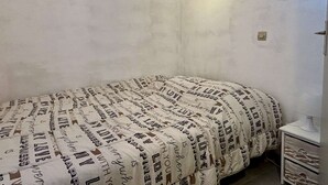 A bedroom with a bed covered in a patterned blanket, a small bedside table, and a wall-mounted light fixture. - Cozy studio - pets allowed, parking (Argelès-sur-Mer)