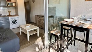 A compact living space with a kitchen, a dining area with a table and chairs, a washing machine, and a small seating area. - Cozy studio - pets allowed, parking (Argelès-sur-Mer)