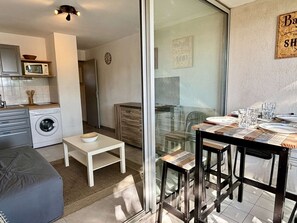A compact living space with a kitchen, a dining area with a table and chairs, a washing machine, and a small seating area. - Cozy studio - pets allowed, parking (Argelès-sur-Mer)