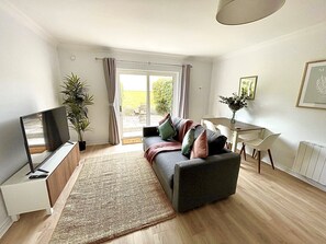 A living room with a sofa, TV, and a dining area with chairs and a table. - Luxury By The Coast 7 (Galway)